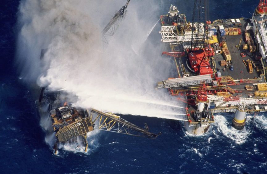 The remains of the Piper Alpha Platform burning as the fire-fighting vessel Tharos, tries to extinguish the flames.