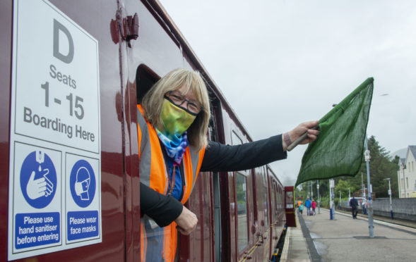 A member of staff on the Jacobite Steam train leaning out the window, while the train is stationary.