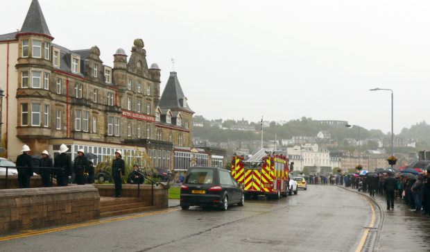 A guard of honour is formed for Brian MacDonald as a sole piper and mourners watch on.