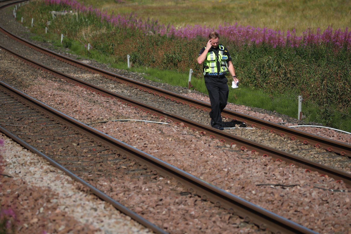 A police officer walks along the tracks at Carmont crossing.