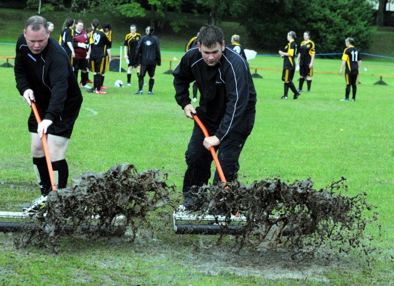 Two men clearing water from the pitch before a match