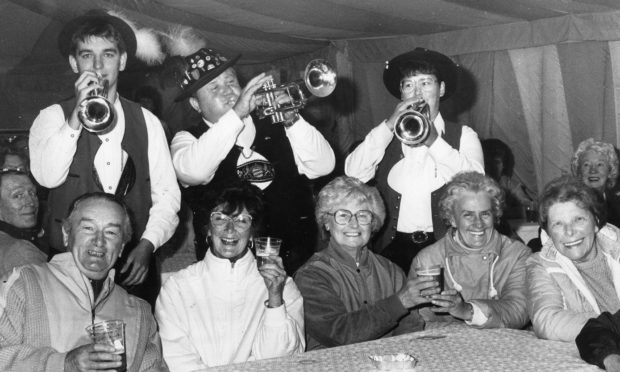 Members of a band playing instruments with people sat at tables during Aberdeen Regensburg Week