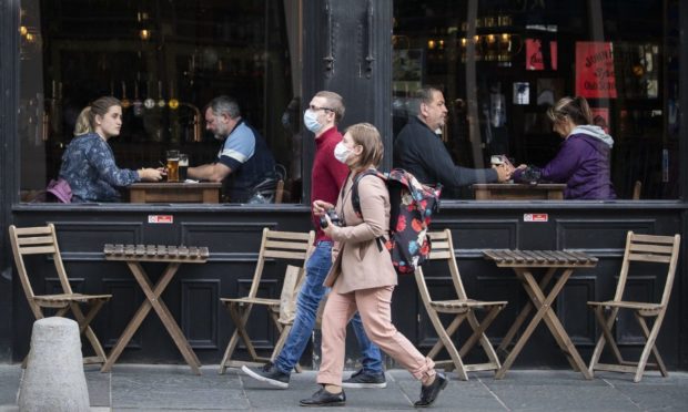 People wearing protective face masks walk past a bar.