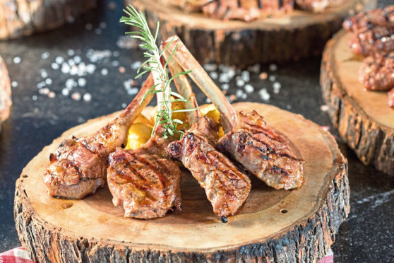 Beautifully grilled lamb rib chop steaks, medium rare with fried potato chips on wood serving board.