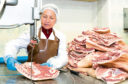 A meat plant worker preparing raw meat for processing and cutting.