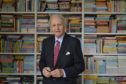 Alexander McCall Smith has had an application to fit solar panels approved. He is standing in front of a library of books.