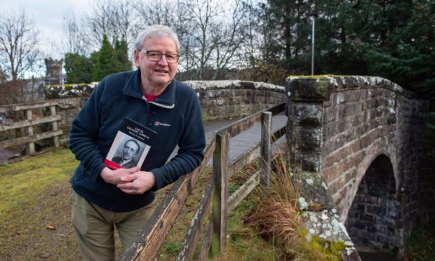 Dr William K Malcolm poses with his book on a bridge near his home in Aberlour