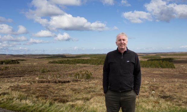 Calum MacDonald with Point and Sandwick Trust's Beinn Ghrideag turbines in the background.