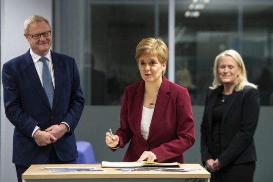 EMBARGOED TO 0001 MONDAY NOVEMBER 23 
Scotland's First Minister Nicola Sturgeon  flanked by  Scottish National Investment Bank CEO Eilidh Mactaggart and chair Willie Watt signs a visitors book at the bank's official launch at their headquarters in Edinburgh, Scotland. PA Photo. Picture date: Thursday November 19, 2020. Photo credit should read: Andy Buchanan/PA Wire