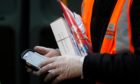 A Royal Mail employee wears gloves as he holds parcels and a handheld device.