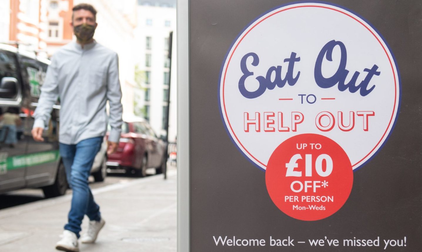 A man walks past an Eat Out To Help Out sign.