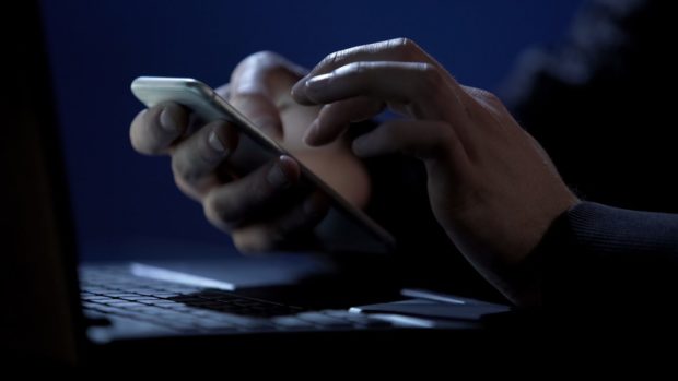 Scammer holds smartphone, cracks two-factor authentication, steals money online; Shutterstock ID 1038184249; Purchase Order: -