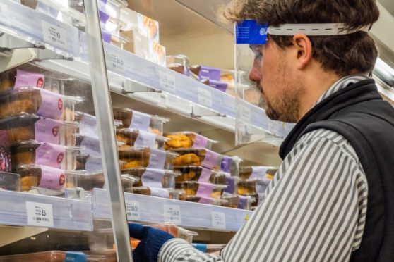 A worker stacks supermarket shelves wearing a face mask. Photo by Guy Bell/Shutterstock