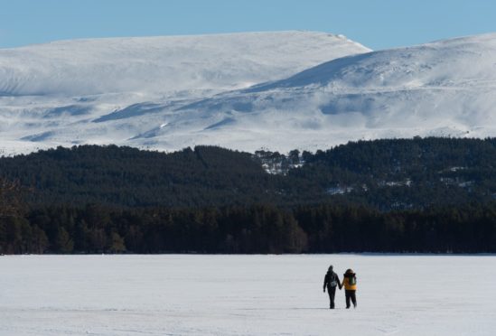Valentina Benacchhini and (yellow Jacket) and Mattia Zenere from Italy who work locally at a hotel walk on and rest by a beautiful frozen Loch Morlich in Aviemore.