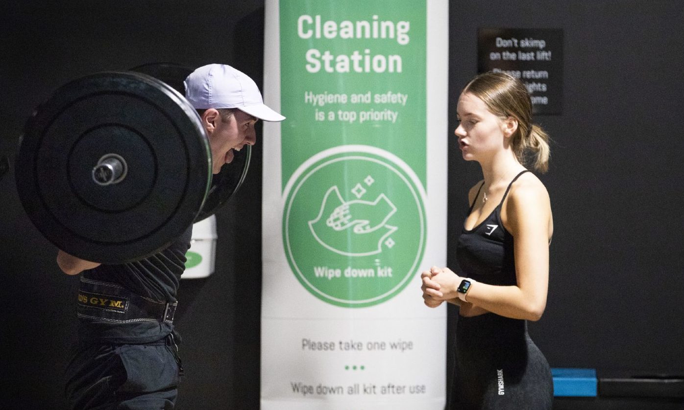 Gym members work out beside a PureGym cleaning station.