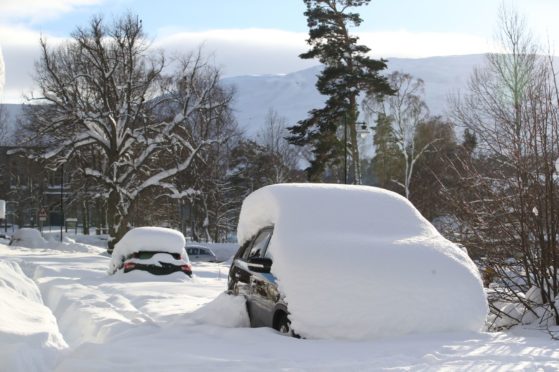 Snow-covered cars parked on the street in Braemar.