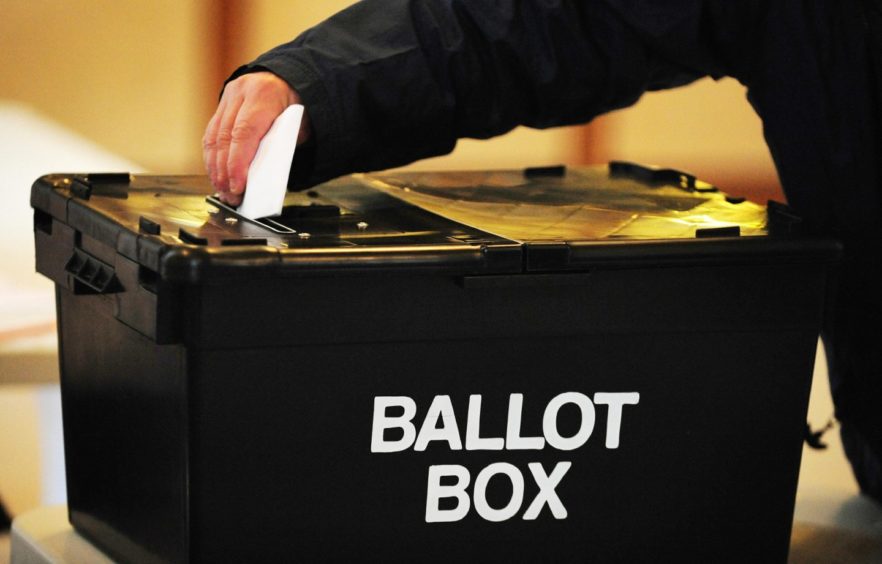 Someone placing a slip of paper into a black ballot box