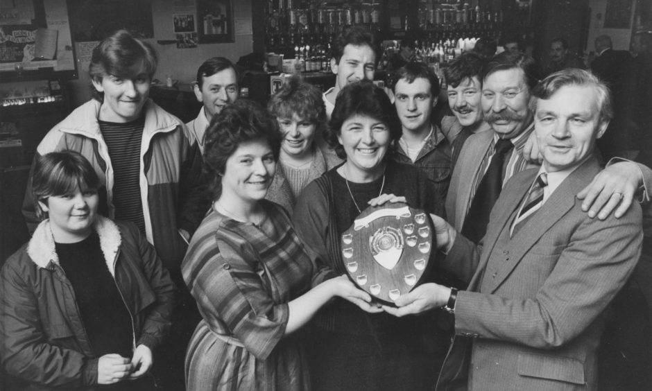 The Lord Byron Bar at Northfield won the Royal National Institute for the Blind competition for the biggest pile of pennies to be collected for institute funds in 1984. Bar staff Norah Gribble and Georgie Boyle were presented with the Andy Stewart Shield watched by bar manager Sandy Cruickshank and customers.