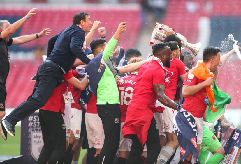 Derek Adams jumps on the back of the Morecambe players celebrating their play-off win.