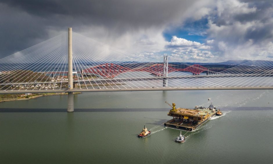 The Iron Lady barge with its cargo of a topside drilling platform for decommissioning being towed by Forth Ports tugs at the Forth Bridges into The Port of Rosyth. Airbourne Lens
