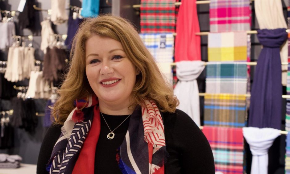 Jenny Urquhart smiling at camera with fabric on wall behind. 