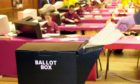 A dummy ballot paper is fed into one of the collapsable plastic ballot boxes designed for the Mayor of London and the London Asssembly elections, due to take place on May 4 2000, while vote counters at Hammersmith Town Hall in the West Central Constituency of London perform a count rehearsal, February 2000.