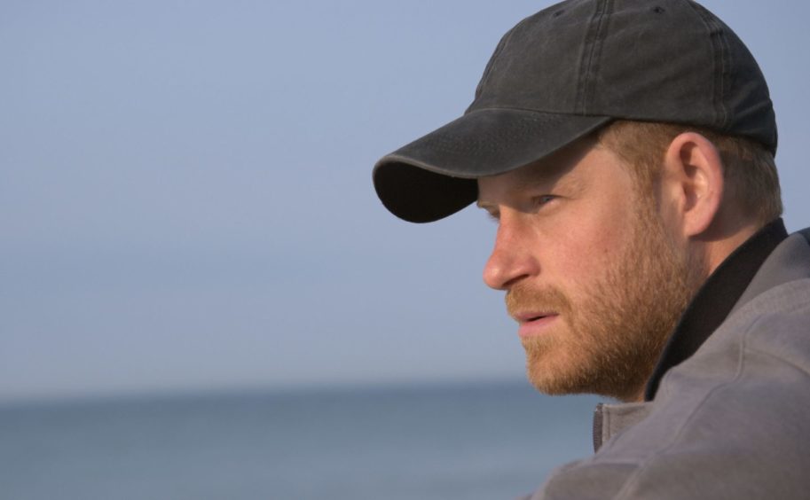 Prince Harry with a cap on staring into the distance. 