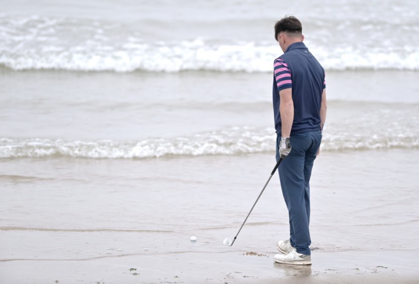 Jack Broun, of Turnberry, contemplates wet feet after his tee shot from the first landed in the waves of Nairn Beach in the stroke play section.