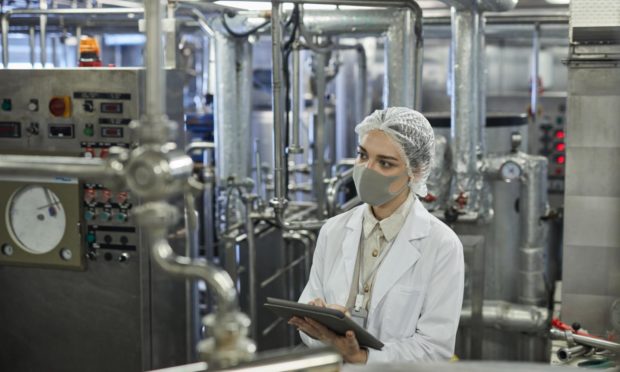 Employee wearing mask and holding digital tablet during 
 a food factory quality control inspection.