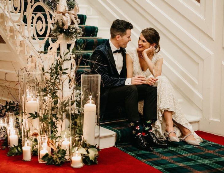 A bride and groom chat on the stairs holding drinks