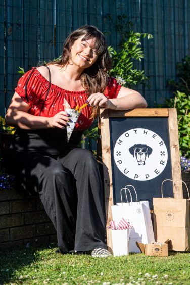 Toni Gordon sitting next to a Mother Pupper sign holding her vegan dog treats