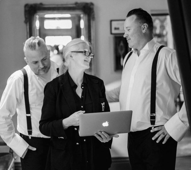 A black and white shot of Alice, the wedding planner chatting to two men