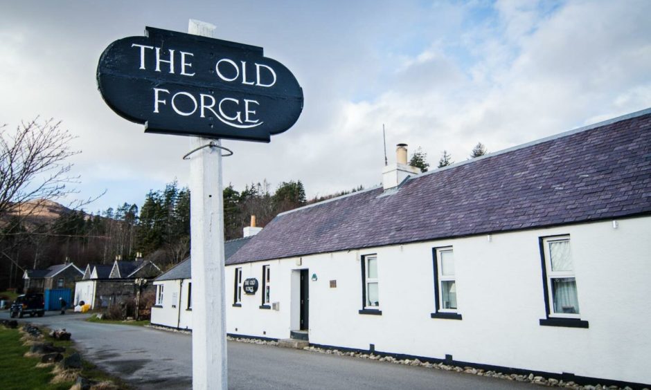 The Old Forge Inn in Knoydart is a long white single story building that has a simple black and white sign outside that reads The Old Forge. 