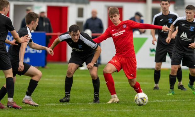 Brora's Matthew Wright, in red, tries to evade Strathspey defenders