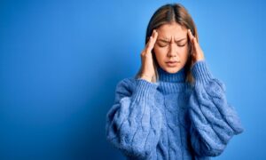 Woman in blue jumper looking stressed next to a blue wall