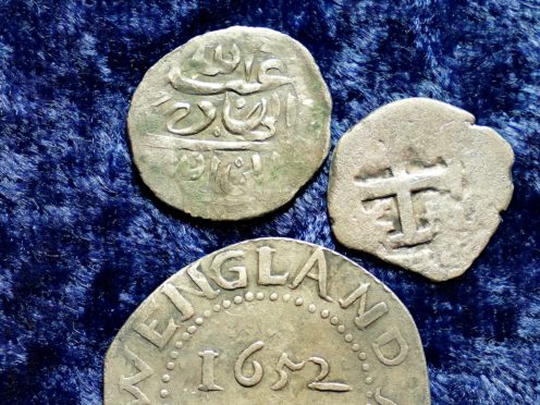 A 17th-century Arabian silver coin, top, that research shows was struck in 1693 in Yemen, rests near an Oak Tree Shilling minted in 1652 by the Massachusetts Bay Colony, below, and a Spanish half real coin from 1727, right, on a table, in Warwick, Rhode Island (Steven Senne/AP)