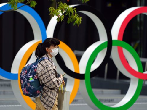 A woman wearing a protective mask walks in front of the Olympic Rings in Tokyo (Eugene Hoshiko/AP)