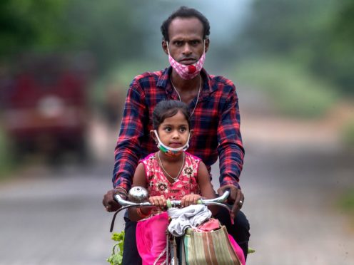 An Indian villager and a child wearing masks ride on a bicycle on the outskirts of Gauhati, India (Anupam Nath/AP)