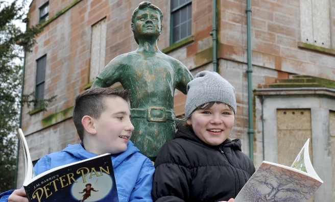 Reign Bowran and Darija Bugaite swap stories with a mini Peter Pan statue. Photography courtesy of Peter Pan Moat Brae Trust by Colin Hattersley Photography.