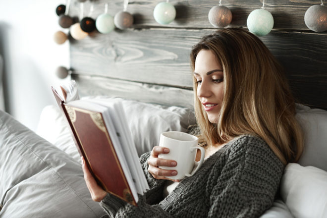 Woman drinking coffee and reading book on bed Featured Image for 3 new wedding books you'll want to read before the big day