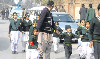 A plainclothes security officer escorts students rescued from nearby school during a Taliban attack in Peshawar, Pakistan.