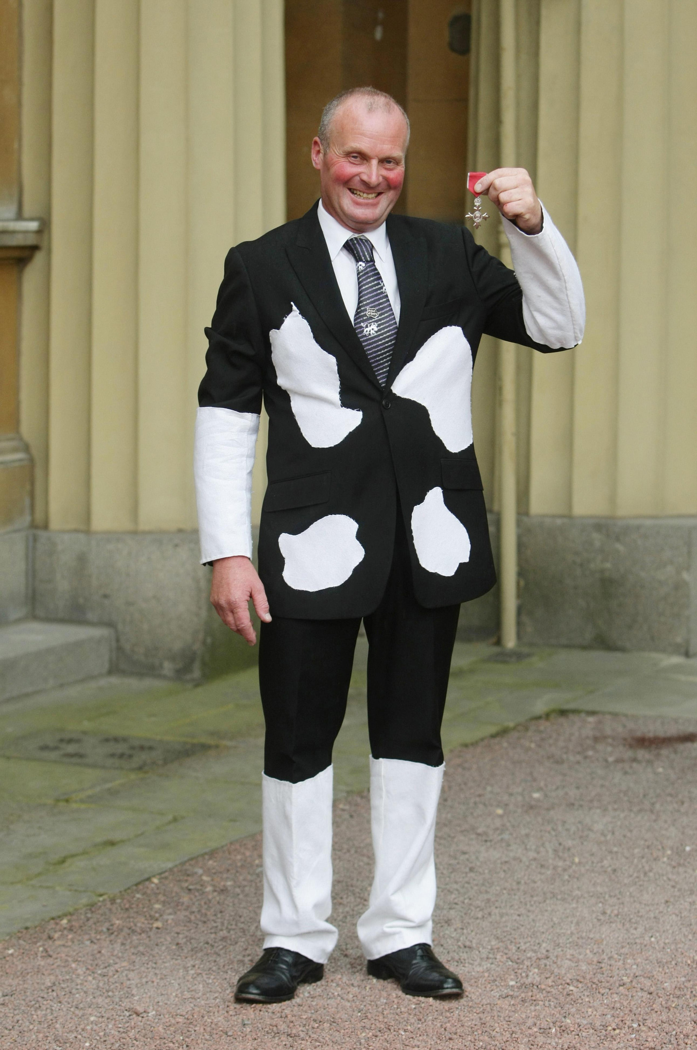 Dressed in a suit resembling a Friesan cow, milkman Tony Fowler holds the MBE he received from Queen Elizabeth II at Buckingham Palace in London (PA)