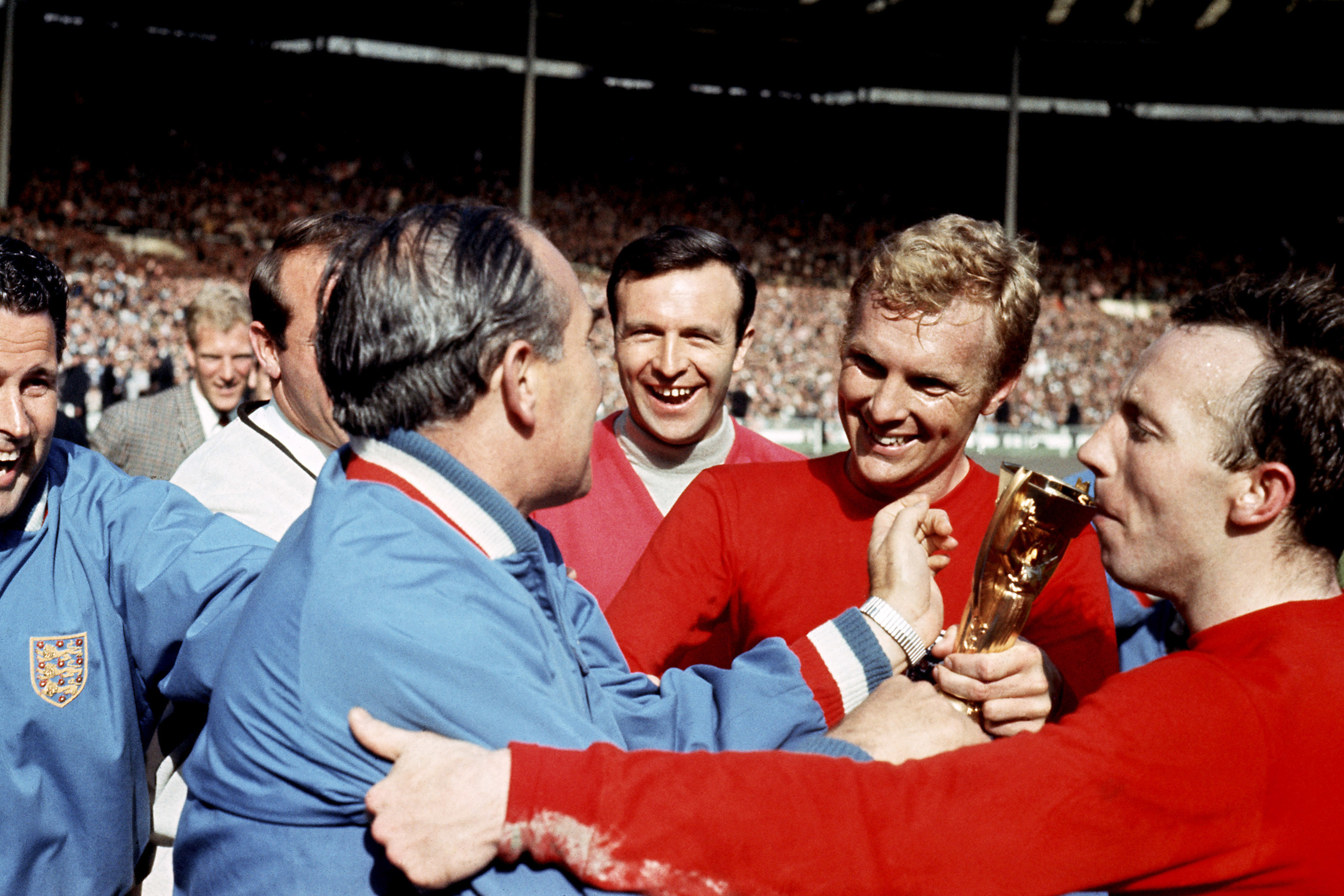 NOBBY STILES KISSES THE TREASURED WORLD CUP TROPHY AS BOBBY MOORE (C) IS CONGRATULATED BY TEAM MANAGER ALF RAMSEY (LEFT IN BLUE) AT WEMBLEY