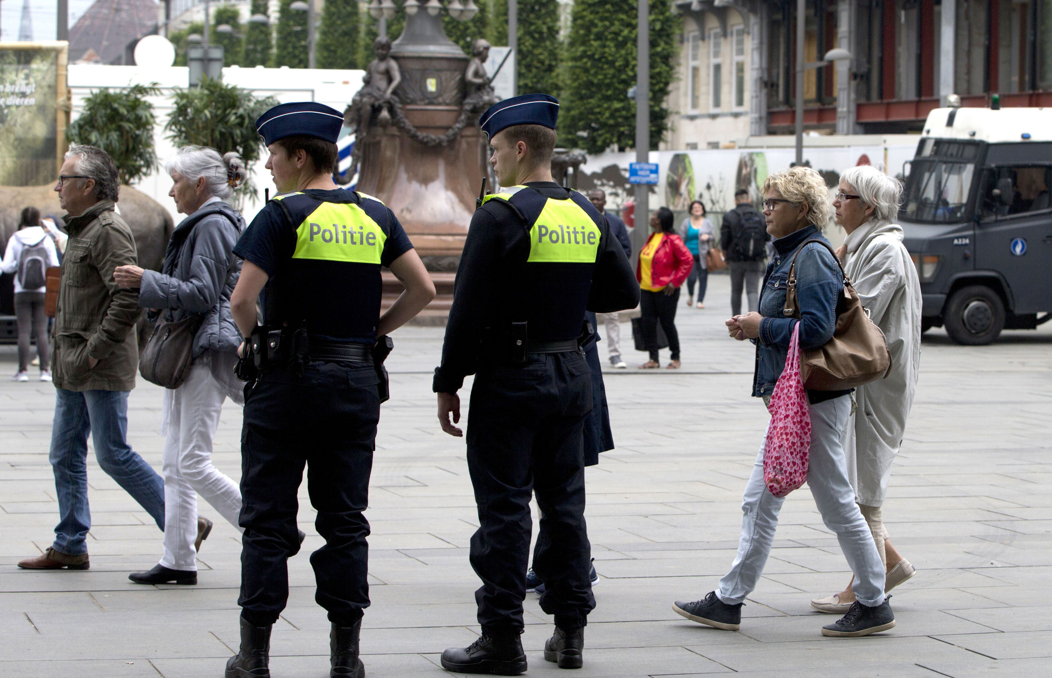 People walk by police standing guard outside the Antwerp Central train station in Antwerp, Belgium on Saturday, June 18, 2016. Police and the bomb squad unit responded to a suspect package in the Antwerp station while the Belgian federal prosecutor's office said early Saturday that homes and car ports were searched in 16 municipalities, mostly in and around Brussels in an anti-terror sweep. (AP Photo/Virginia Mayo)