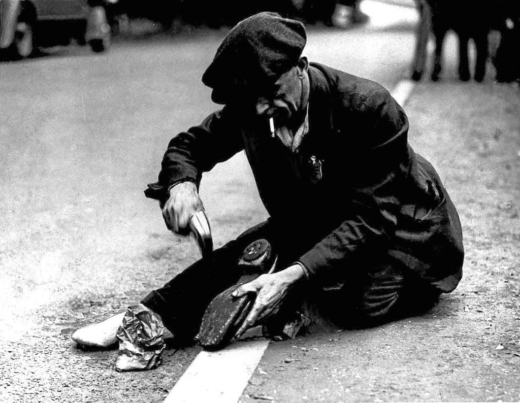 One of the marchers in the Jarrow Crusade halts in the middle of the road to repair his boot 