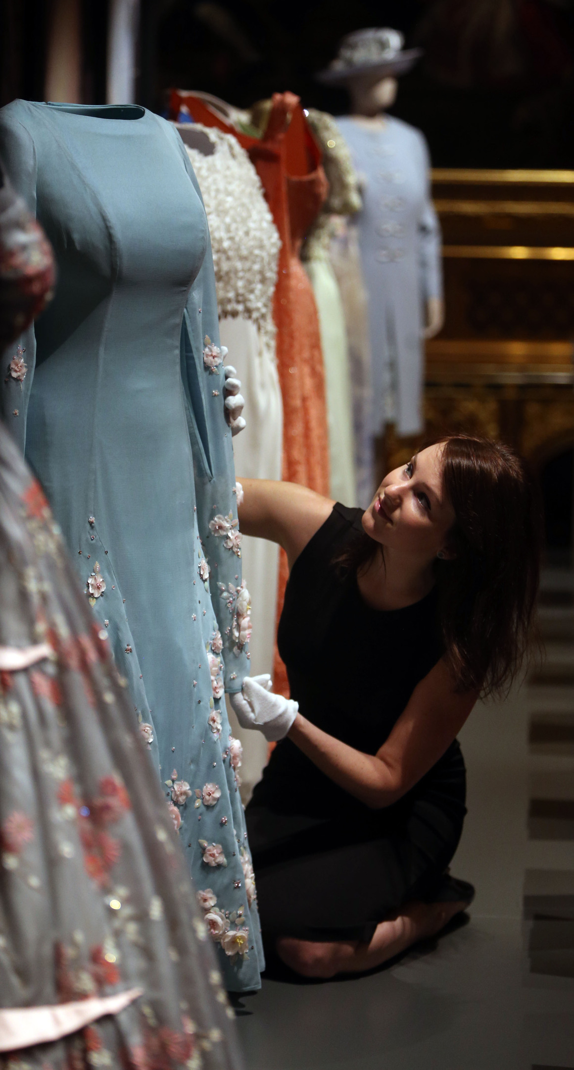 Royal Collection staff member Roxy Gilhooley arranges a selection of dresses worn by The Queen, in the State Dining Room during a press preview for Fashioning a Reign: 90 Years of Style from the Queen's Wardrobe, an exhibition at Windsor Castle in Berkshire (Steve Parsons/PA Wire)
