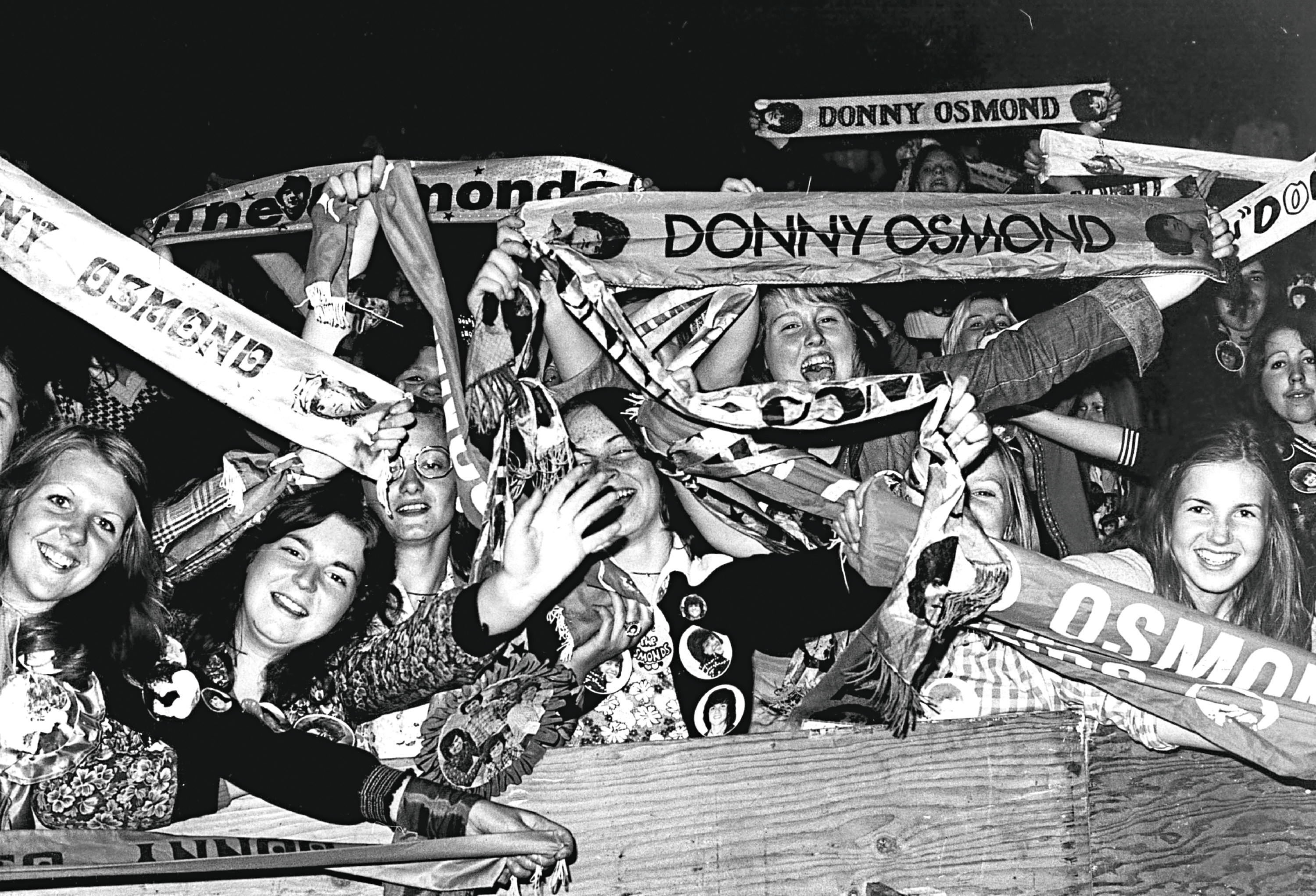 1975: Teenage fans of the American pop group The Osmonds wave scarves emblazoned with the names of their idols. (Photo by Evening Standard/Getty Images)