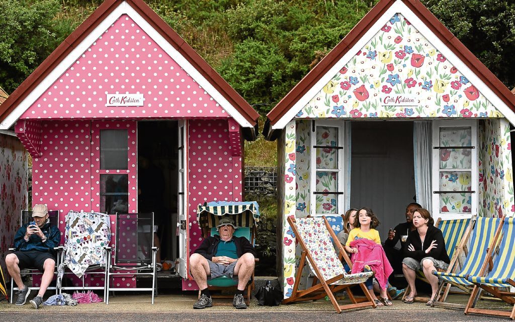 Members of the public sit outside their Cath Kidston designed beach huts on Bournemouth beach (PA)