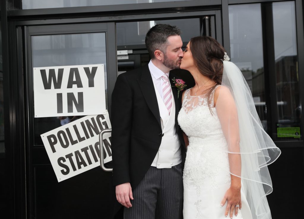Alliance candidate for West Belfast Sorcha Eastwood casts her vote in the 2017 General Election, with her husband, Dale Shirlow, at a polling station in Lisburn, Northern Ireland, still wearing her wedding dress after they were married earlier in the day. PRESS ASSOCIATION Photo. Picture date: Thursday June 8, 2017. See PA story ELECTION Main. Photo credit should read: Brian Lawless/PA Wire