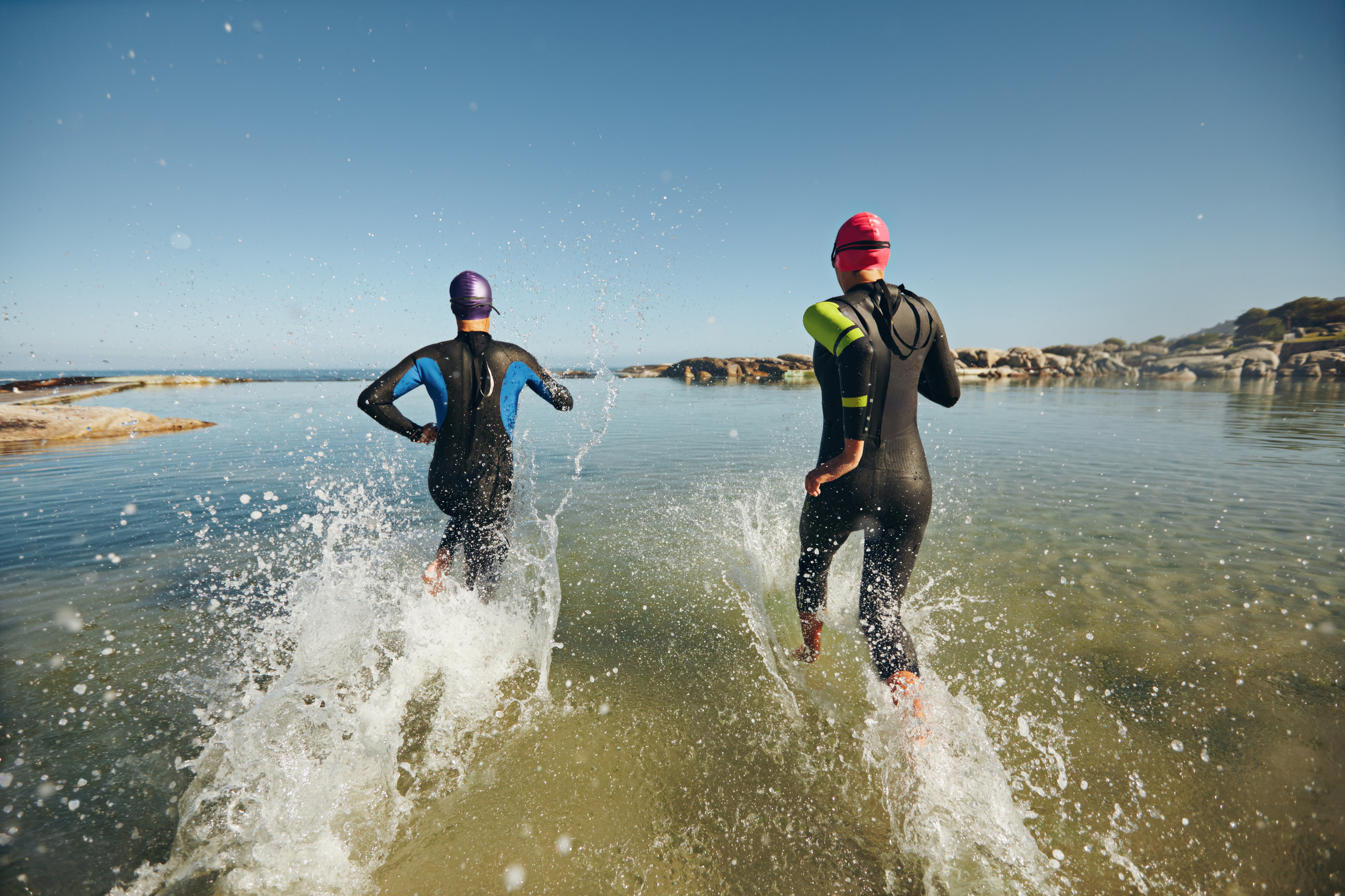 Two athletic swimmers entering the water with their wetsuits on. (iStock)